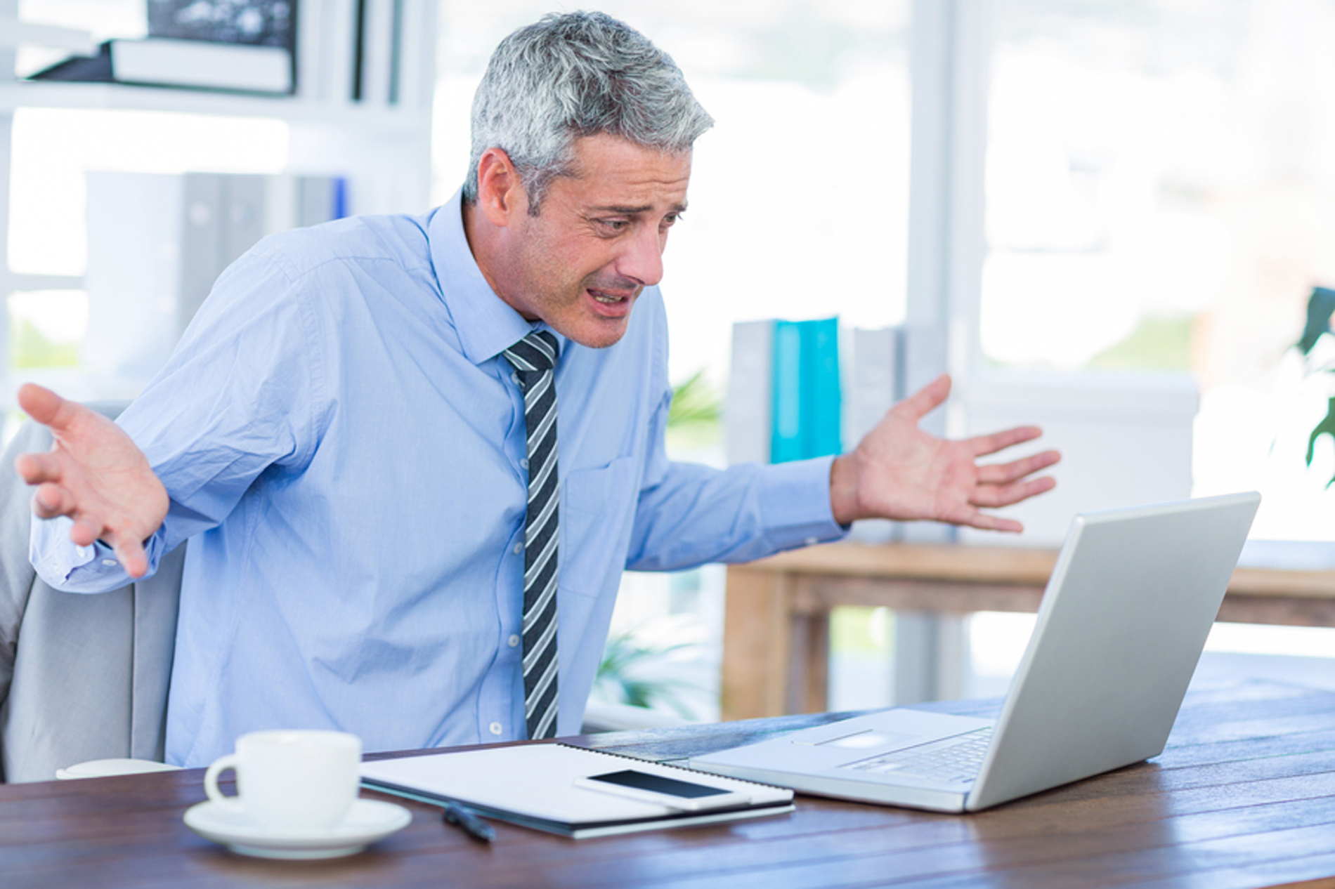 Man in front of his laptop computer appearing frustrated.